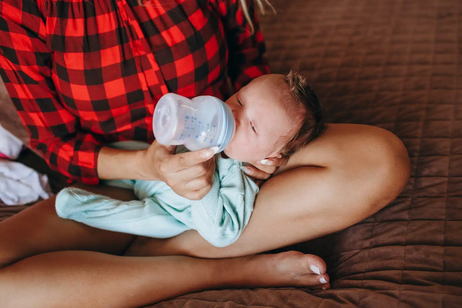 woman in teal tank top drinking milk from feeding bottle